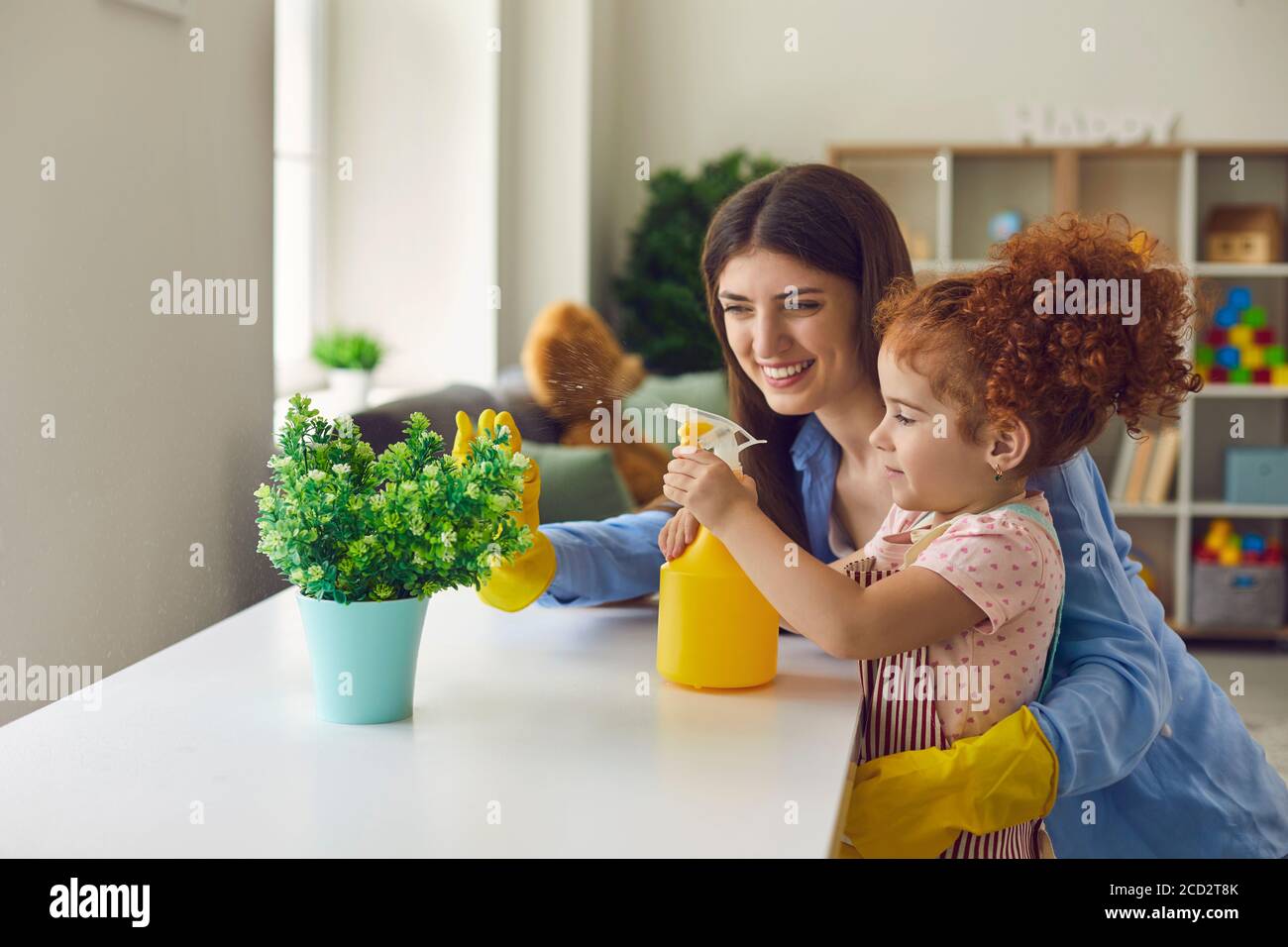 Bella ragazza piccola che aiuta la sua madre acqua houseplant a casa, copia testo spazio. Foto Stock