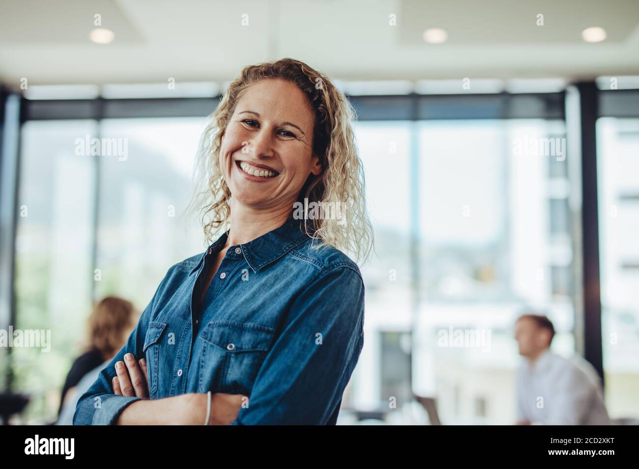 Donna d'affari positiva in sala riunioni con colleghi che discutono in background. Donna professionista al meeting della sala riunioni. Foto Stock