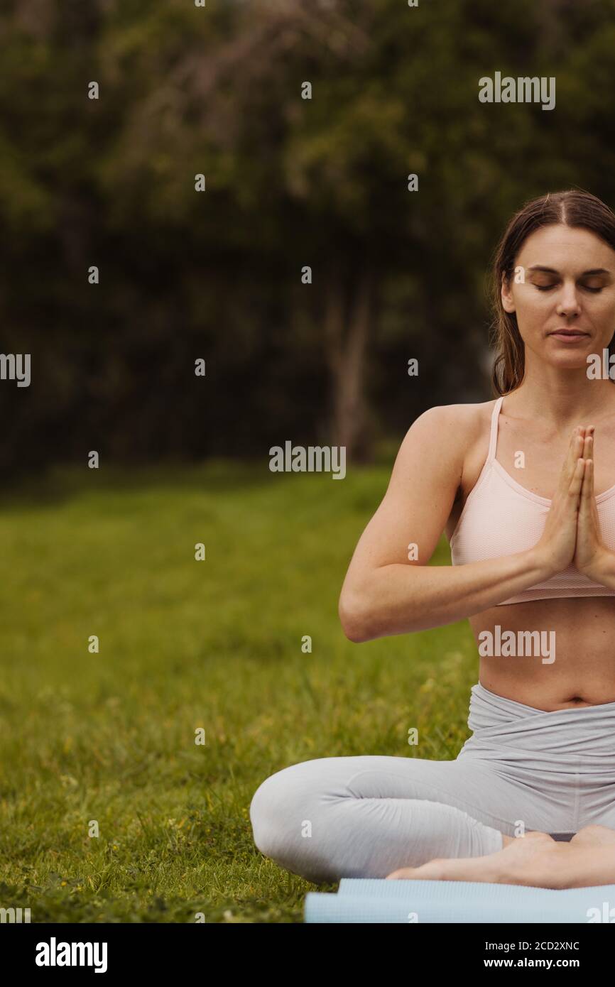 Ripresa tagliata di una donna seduta in una posa yoga con palme insieme. Donna che pratica yoga in un parco. Foto Stock