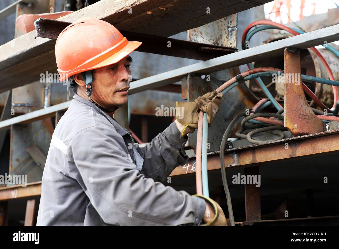 Un lavoratore è occupato a saldare parti di una nave in una fabbrica locale di navi sotto l'alta temperatura, città di Zhoushan, provincia di Zhejiang della Cina orientale, 18 Ju Foto Stock