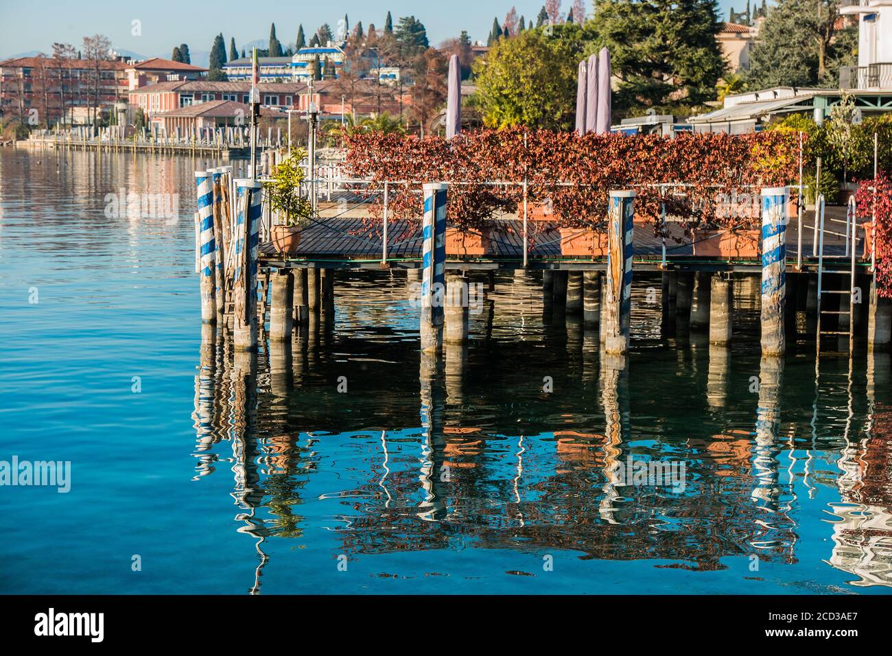 Un antico molo in legno testurizzato e colorato sul Lago di Garda Sirmione. Nell'acqua liscia si riflette il piccolo molo per le imbarcazioni da diporto. Foto Stock