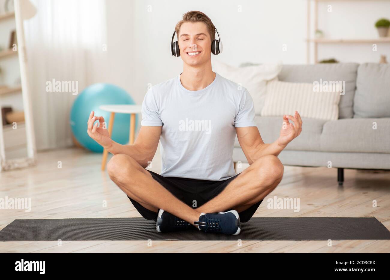 Allenamento moderno con musica a casa. Un ragazzo sorridente in cuffia ama lo yoga e la meditazione Foto Stock