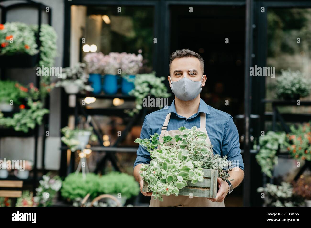 Piccola impresa e inizio della giornata lavorativa. L'uomo in maschera protettiva toglie fuori la scatola delle piante Foto Stock