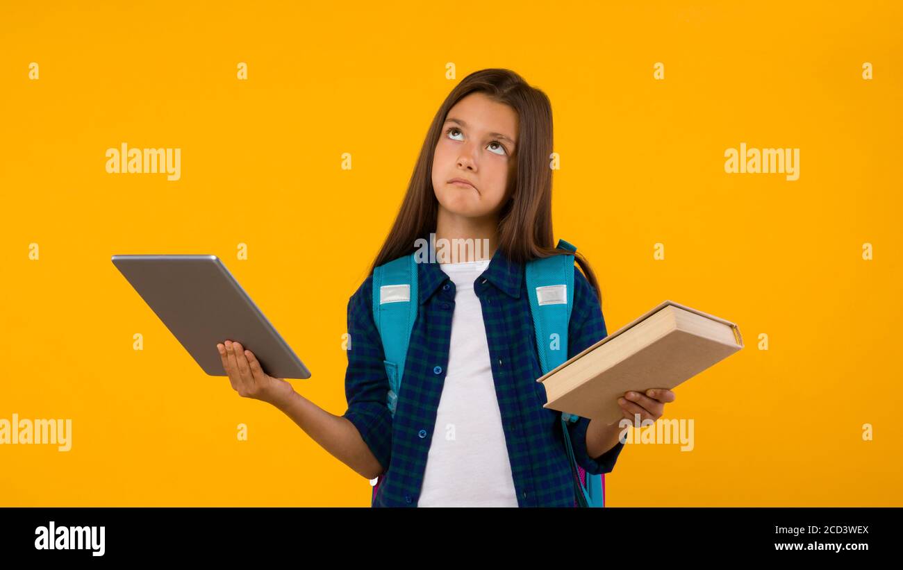 Pensando ragazza in piedi con libro e tablet in studio Foto Stock