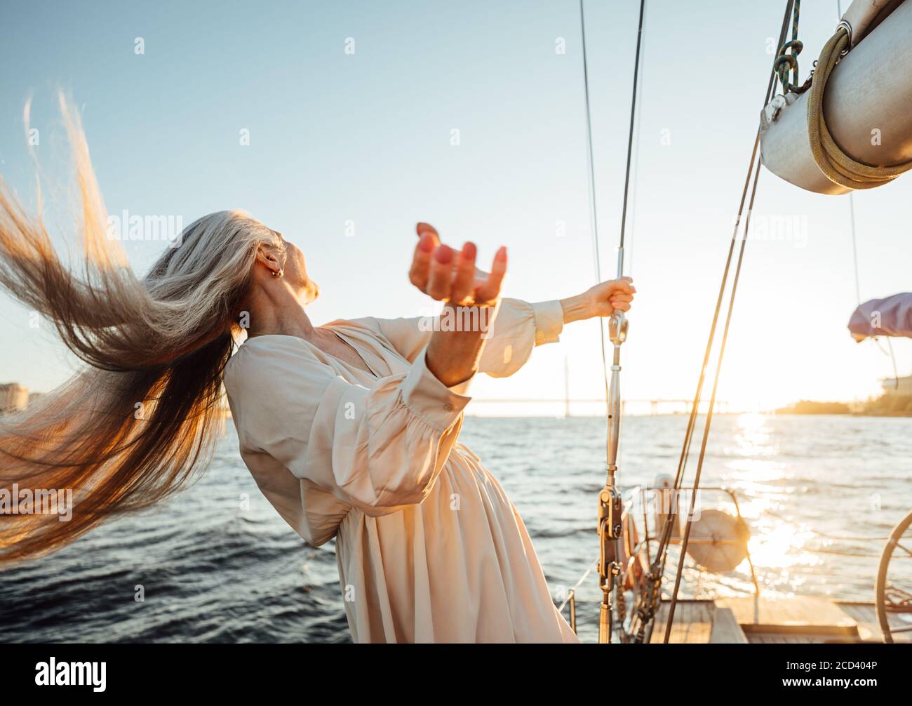 Donna matura irriconoscibile con capelli lunghi che si divertono su un yacht e guardando al tramonto Foto Stock