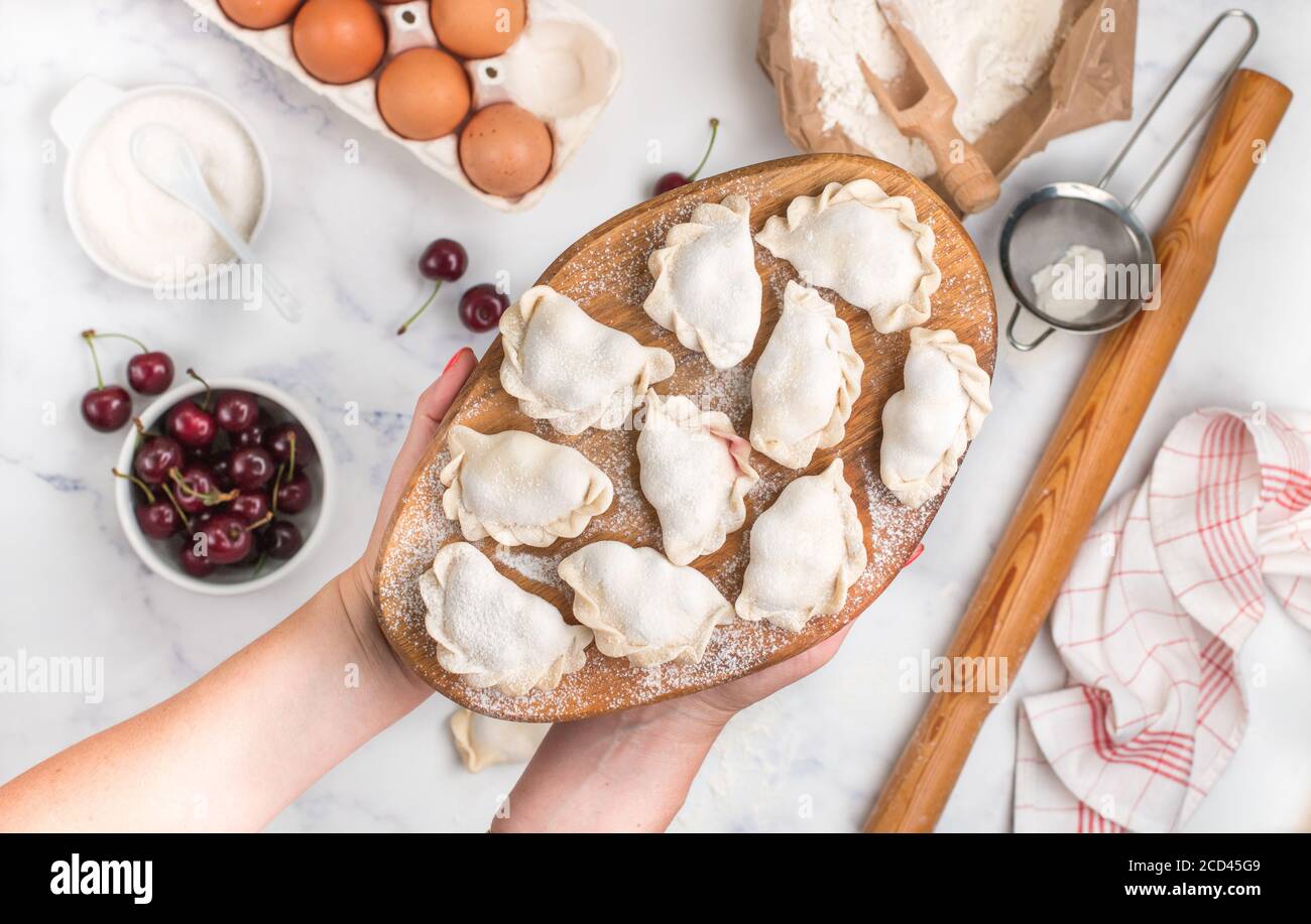 Preparare deliziosi gnocchi dolci con ciliegie. Dessert tradizionale russo e ucraino. Vareniki e ingredienti su fondo marmoreo -farina, Foto Stock