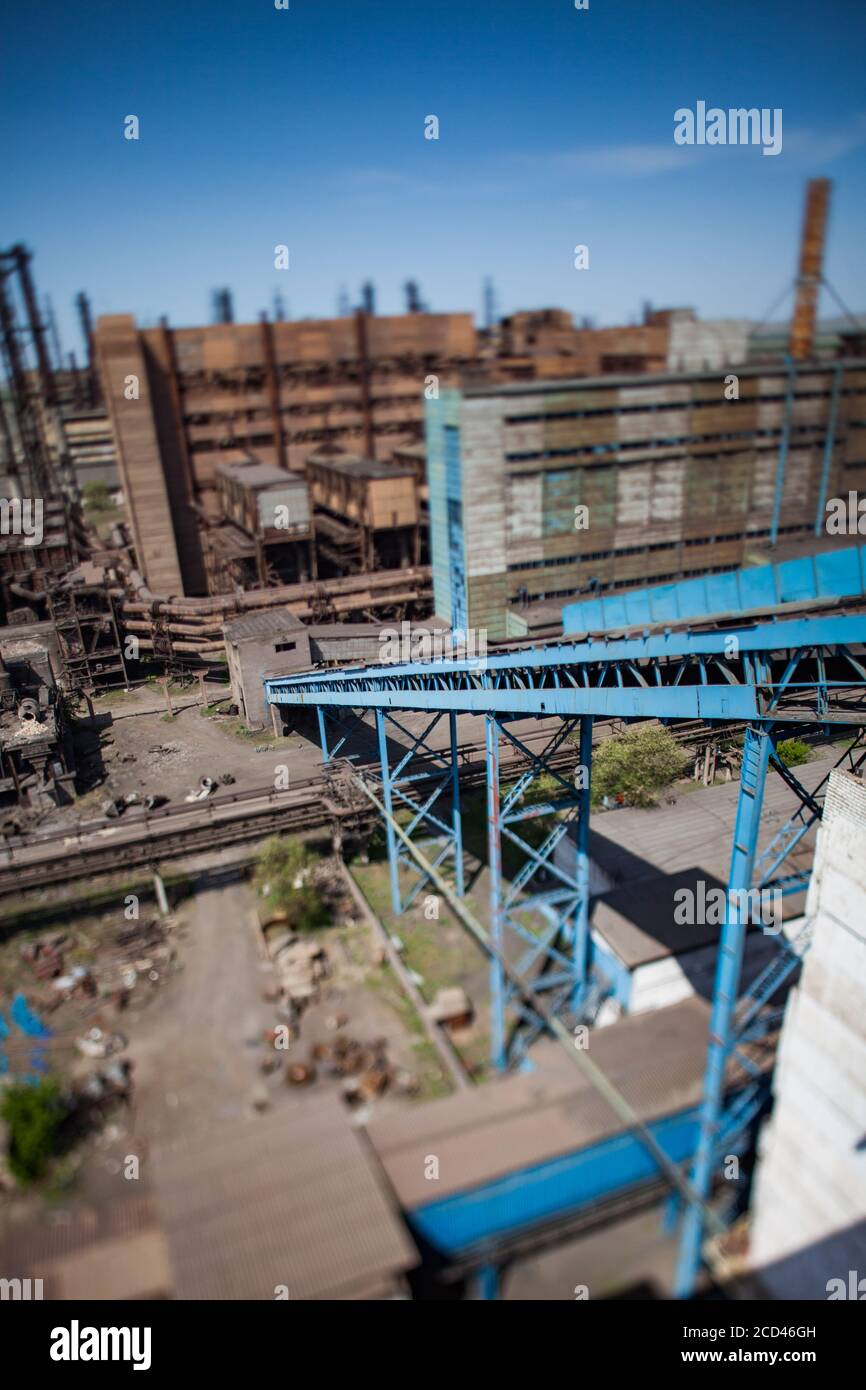 Vecchi edifici della fabbrica di metallurgia con trasportatore blu e camini di fabbrica su cielo blu. Vista dall'alto e obiettivo tilt-shift. Foto Stock