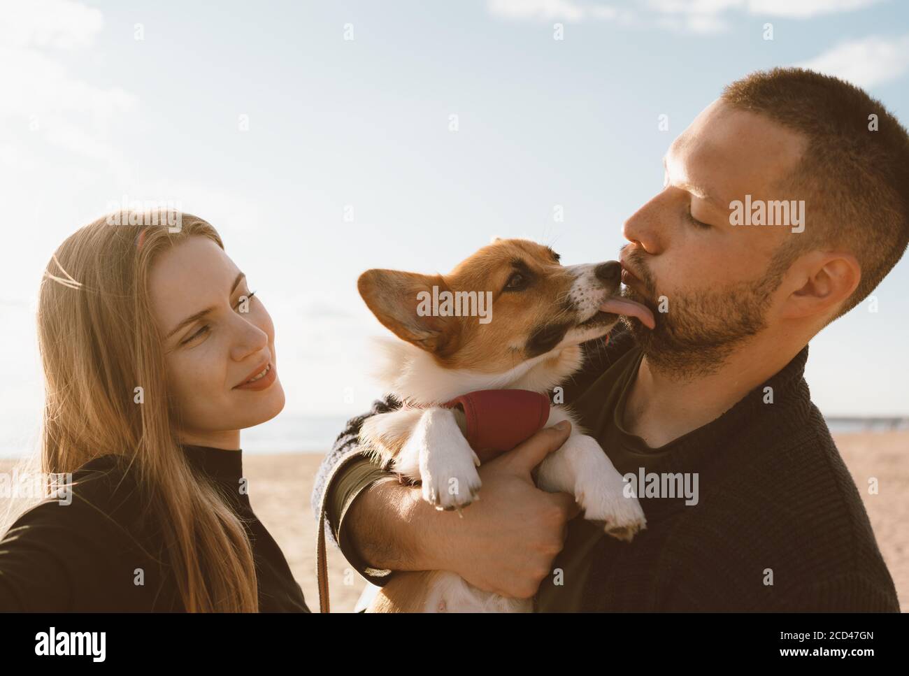 Giovane coppia felice con il cane che scatta foto selfie sulla spiaggia. Bella famiglia e Corgi cucciolo cazzo uomo guancia. Famiglia con animali domestici all'aperto, camminando insieme, marito e moglie si rilassano in estate in mare Foto Stock