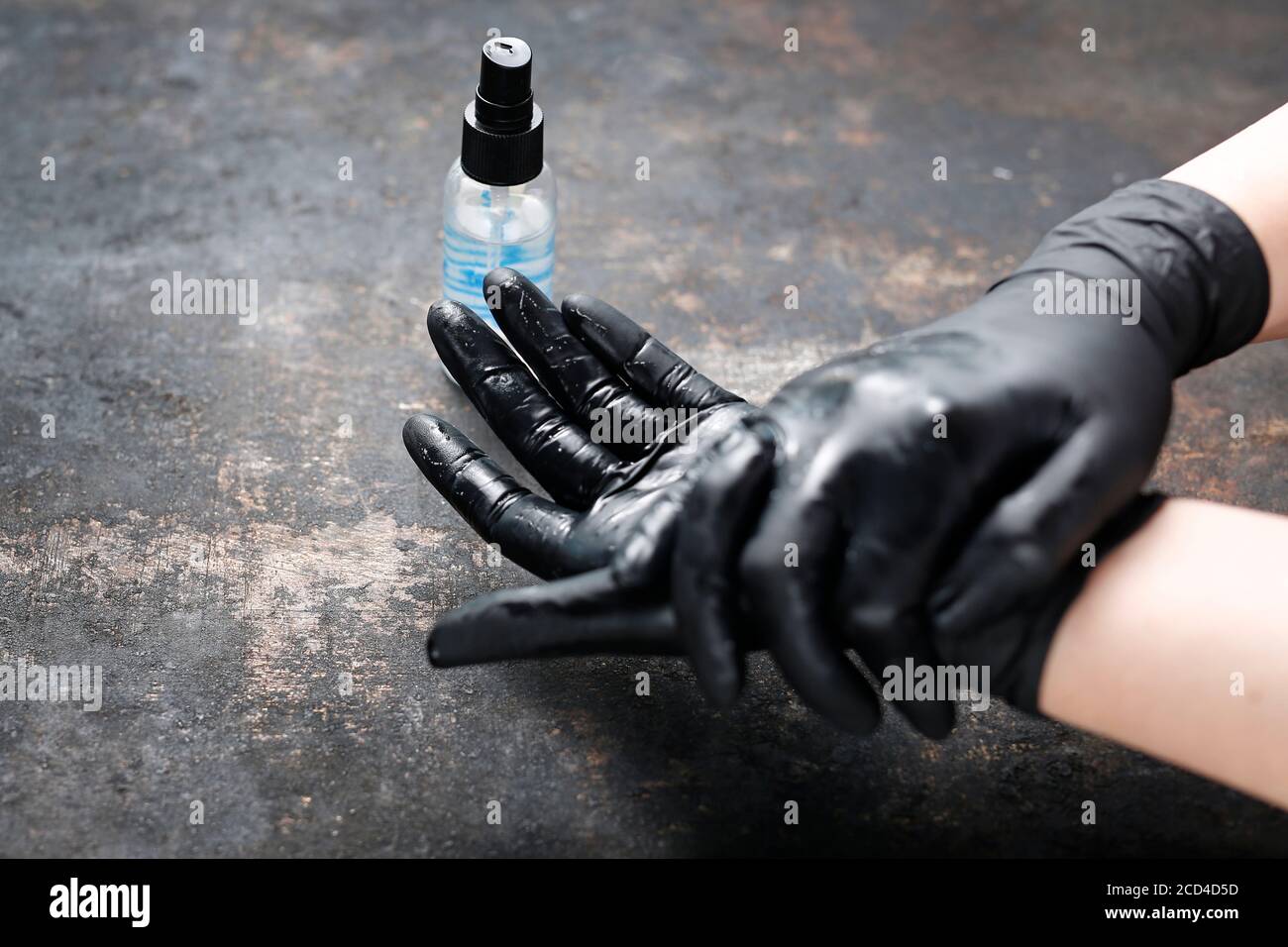Mani in guanti protettivi neri disinfettati con liquido antivirus. Lavarsi le mani con un liquido disinfettante. La donna mostra le fasi della mano corretta Foto Stock
