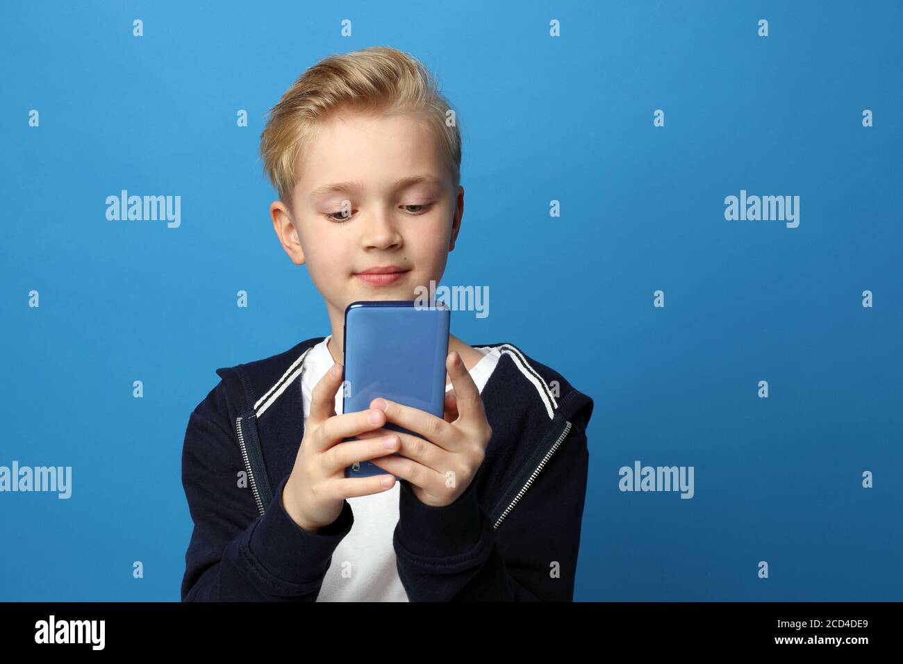 Un bambino che parla con uno smartphone moderno. Divertimento smartphone. Un ragazzo che gioca con uno smartphone.Ritratto di un bambino su uno sfondo blu colorato. Emozioni Foto Stock