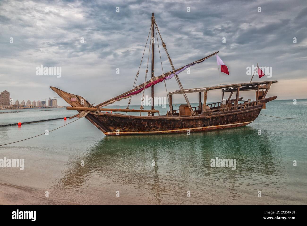 Tradizionale barca di legno (dhow) nel golfo arabo con bandiera Qatar, luce del giorno spara con nuvole nel cielo in background Foto Stock