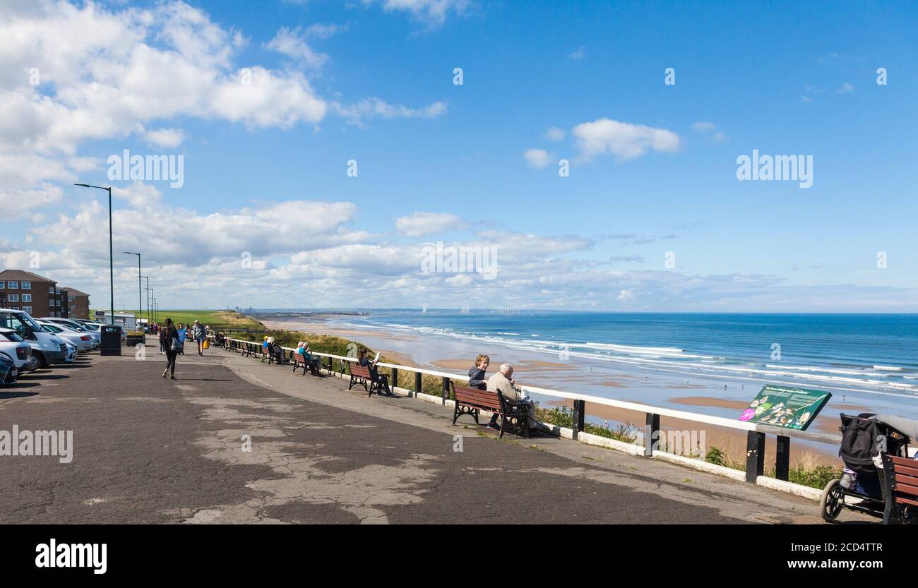 La gente sedette sulle panchine sul lungomare ammirando la vista A Saltburn dal mare, Inghilterra, Regno Unito Foto Stock