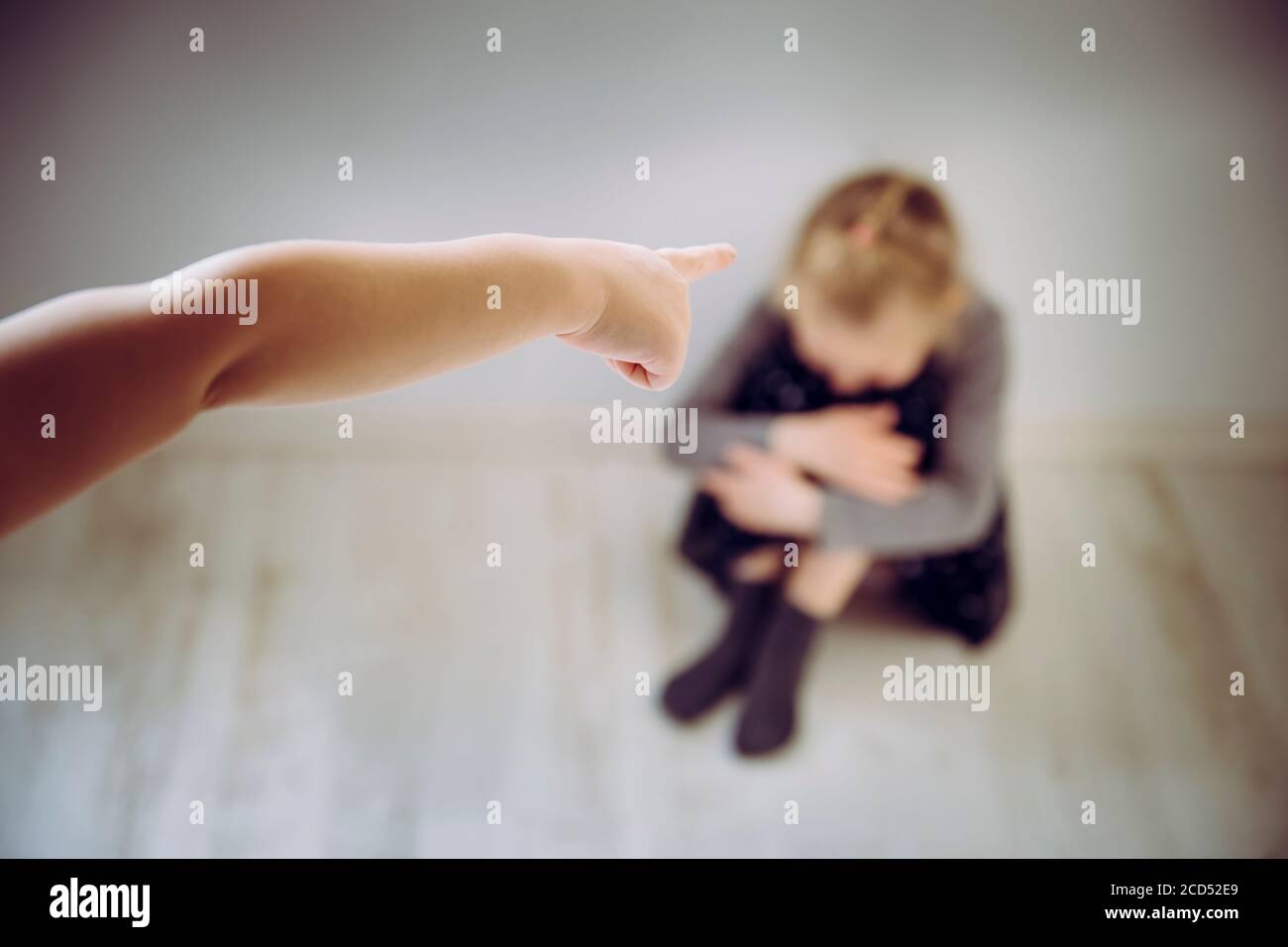 Bambino bullo che punta il dito contro il bambino della vittima sfocato irriconoscibile che si siede sul pavimento e piange. Concetto di bullismo. Foto Stock