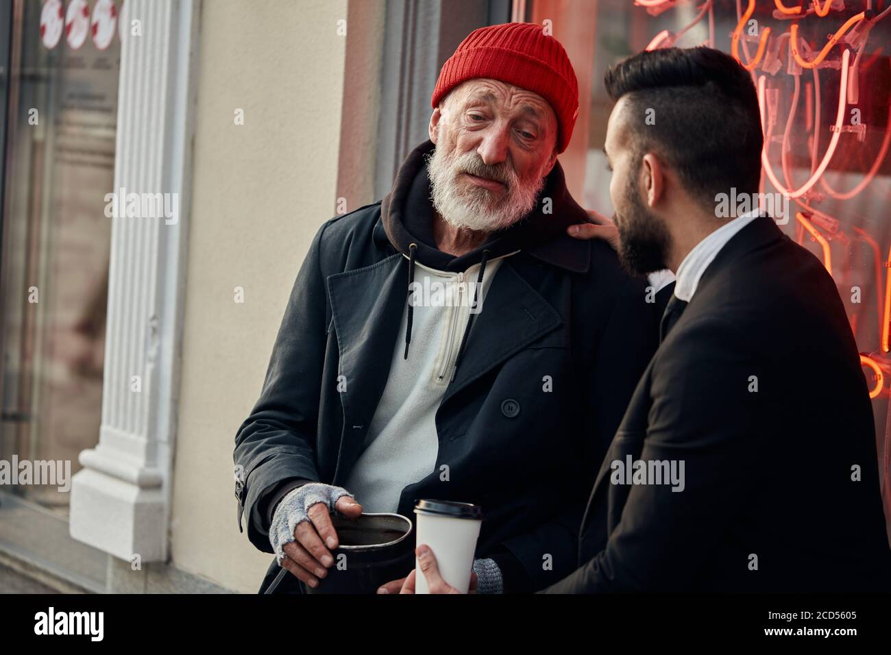 Un ricco uomo reattivo sedette con i senzatetto in strada e parla, ascoltalo Foto Stock