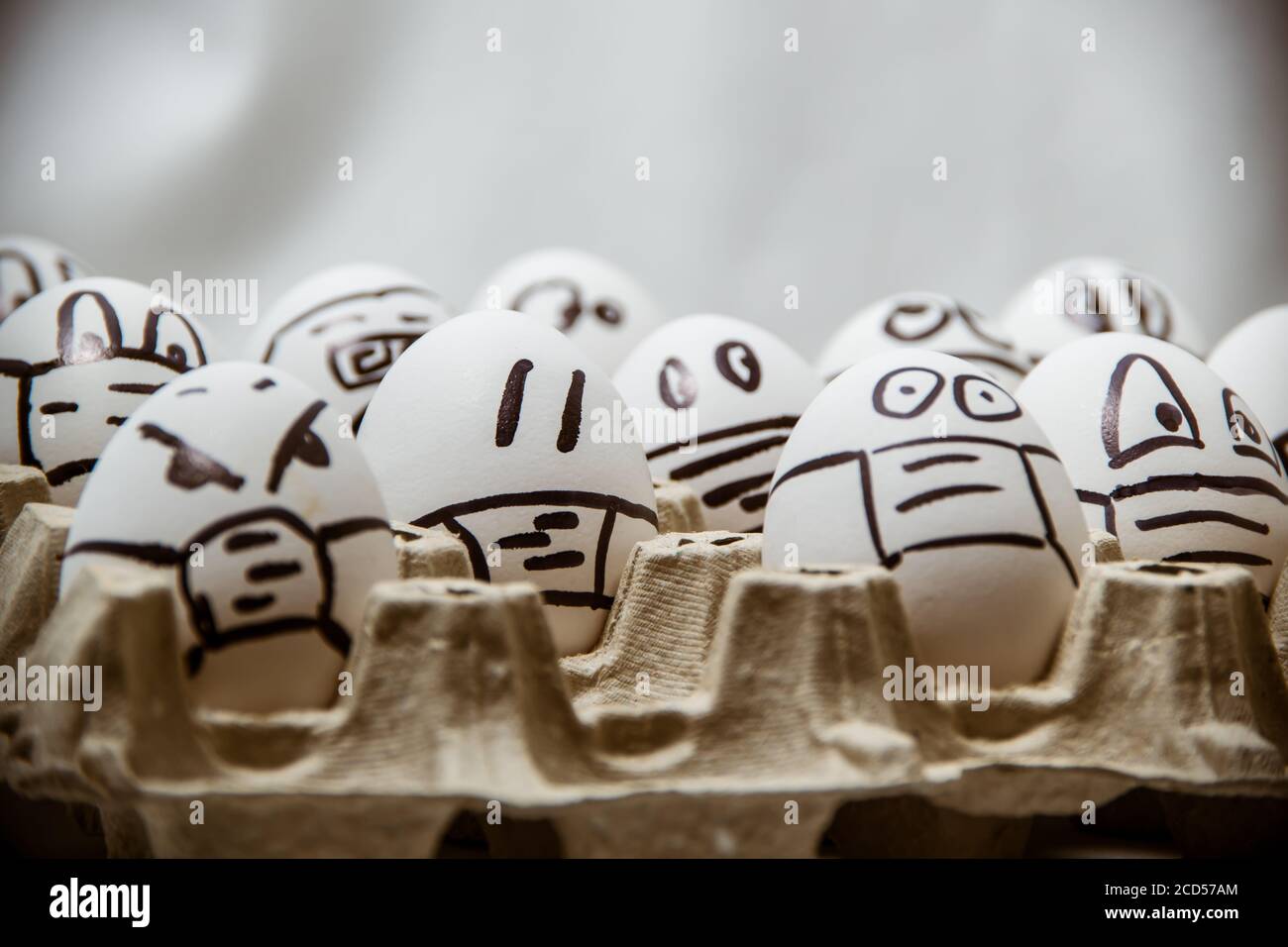 primo piano di diverse uova di pasqua di pollo con doodle facce indossare maschere mediche con sfondo bianco. Foto Stock