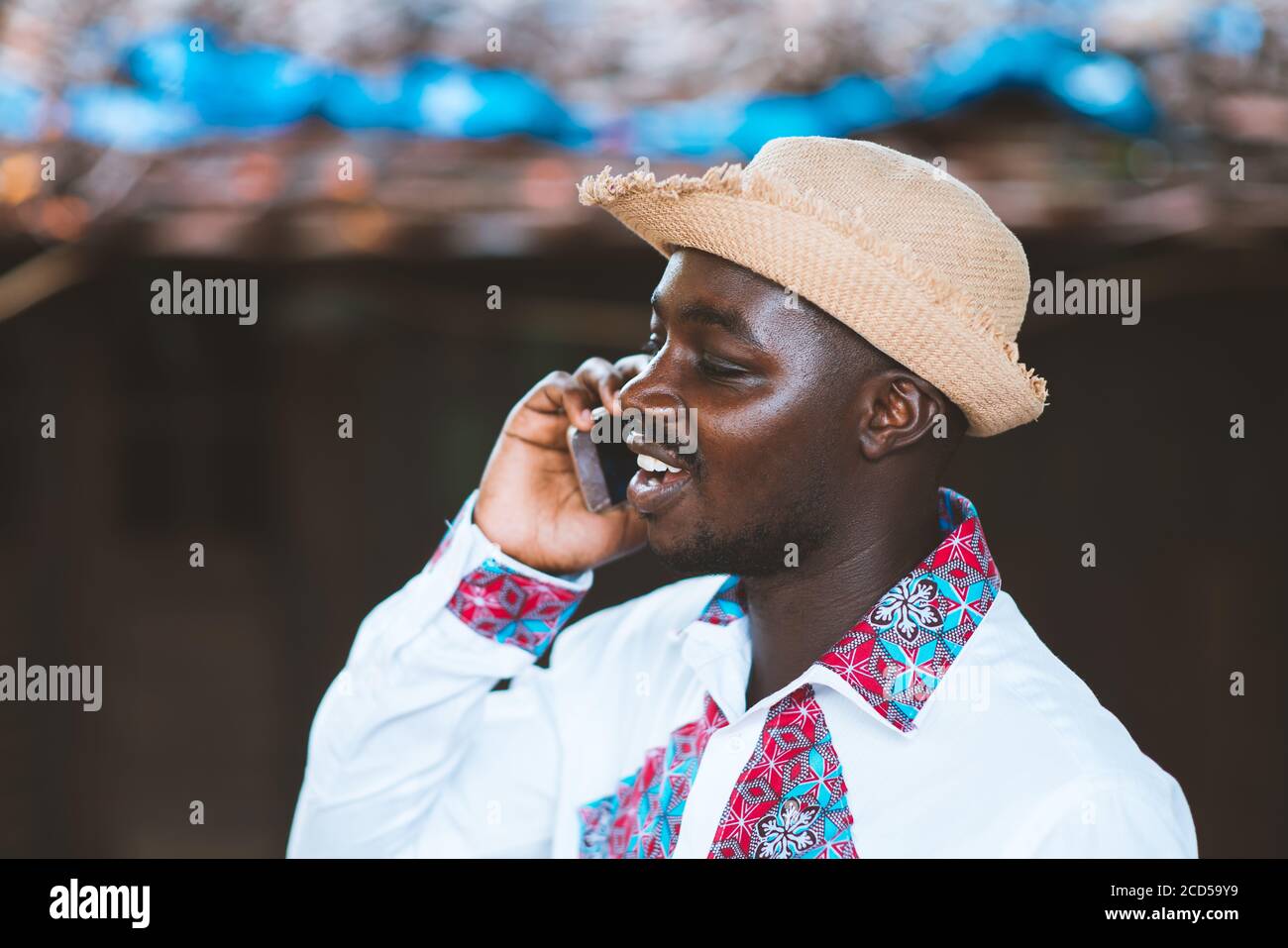 Uomo africano che indossa un cappello e abiti colorati tradizionali  africani con l'utilizzo dello smartphone Foto stock - Alamy