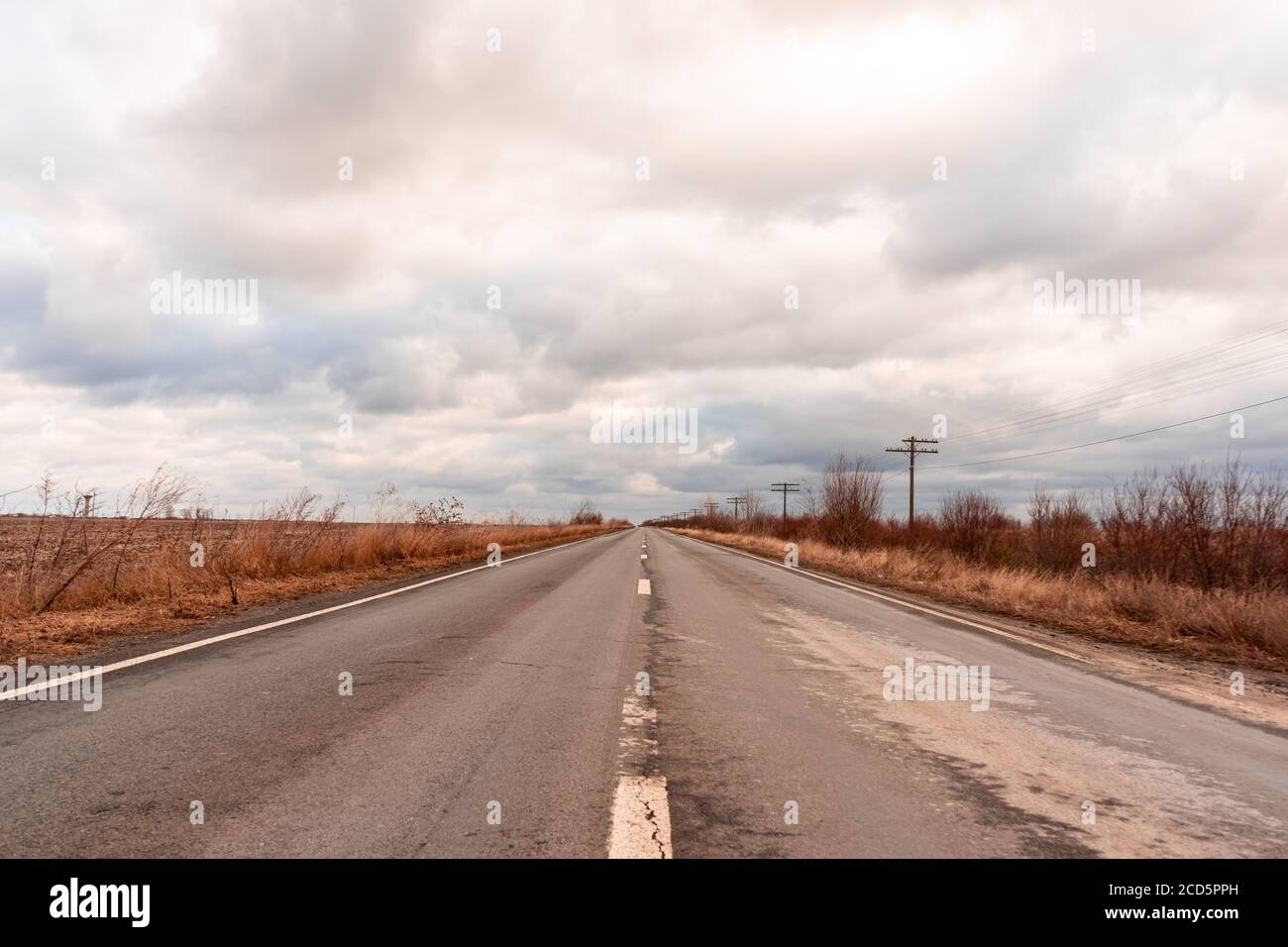 Vista di una strada vuota fuori città. Poli del telegrafo. Nuvole nel cielo. Foto Stock