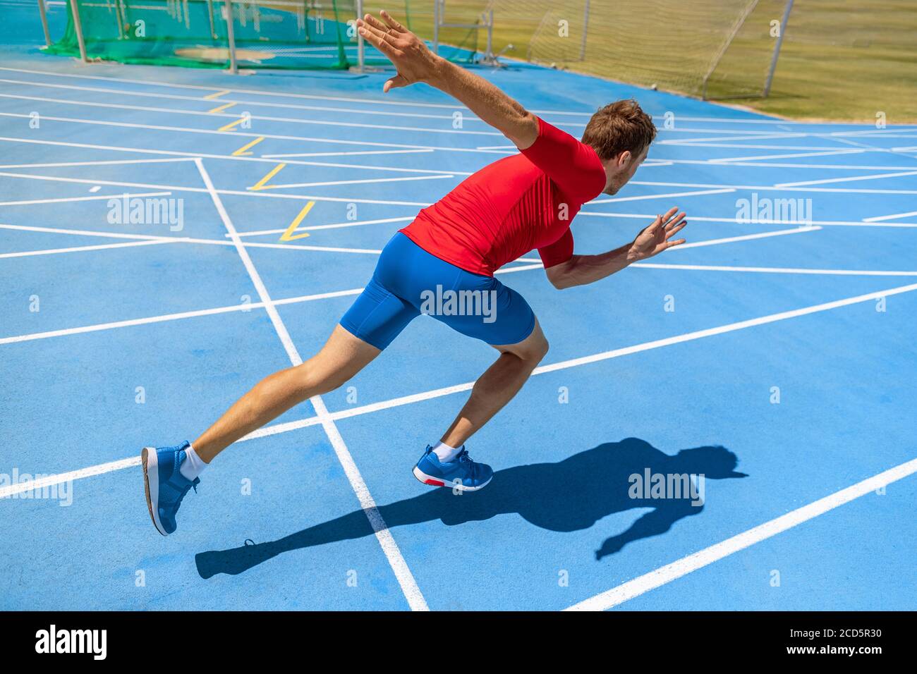 Atleta di runner che inizia a correre all'inizio della pista su piste da corsa azzurre presso l'atletica all'aperto e lo stadio da campo. Sprinter in gara. Sport e. Foto Stock
