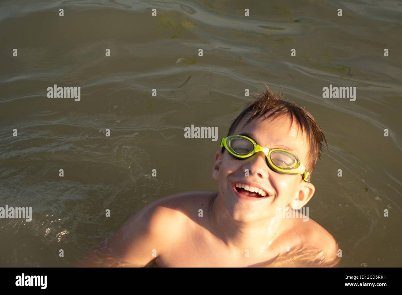 Ragazzo di 10 anni in occhiali da bagno verdi bagna e sorride in mare aperto. Foto Stock