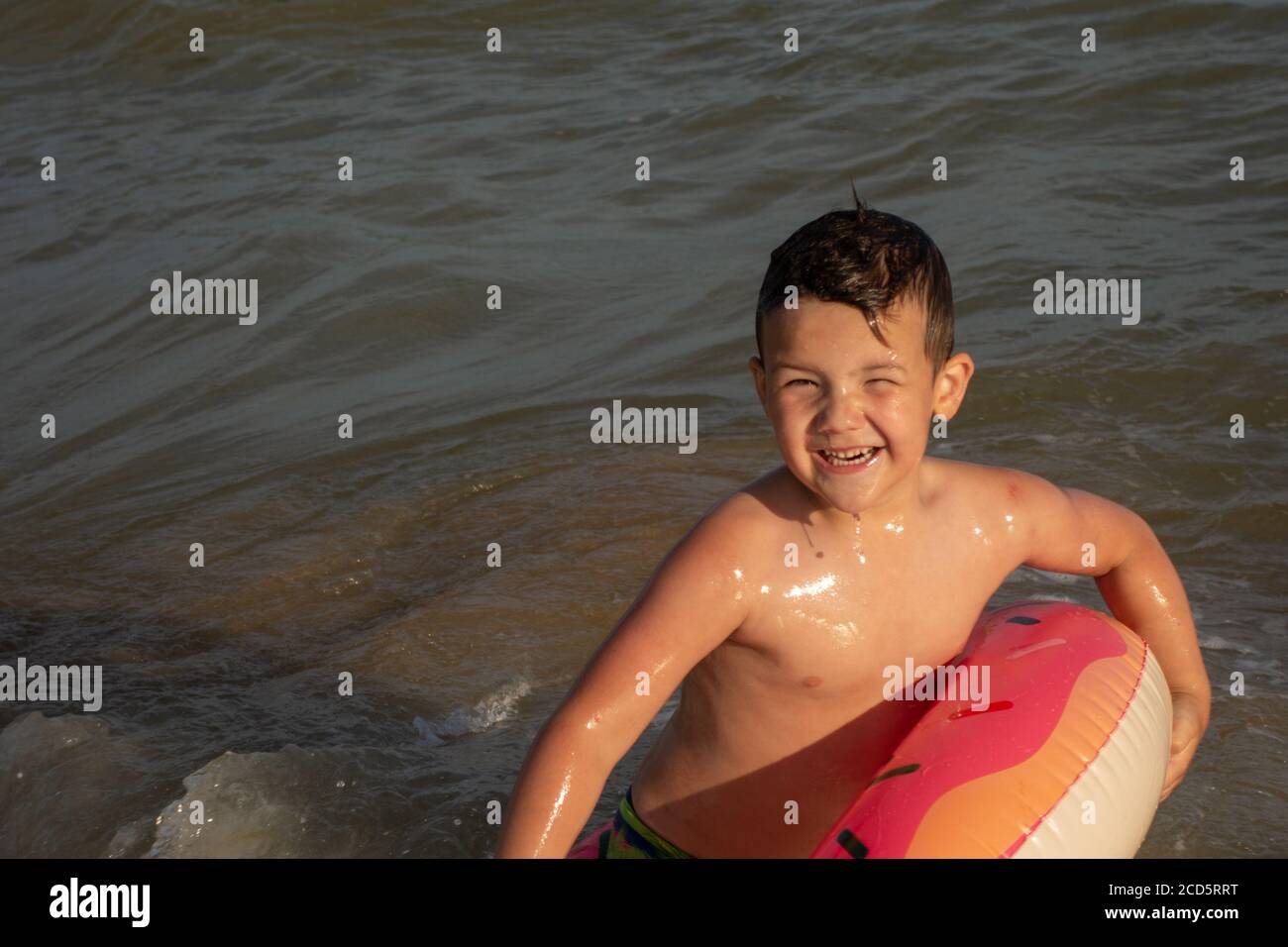 Un ragazzo di 5 anni bagna in un anello di vita a forma di ciambella in una giornata di sole. Foto Stock