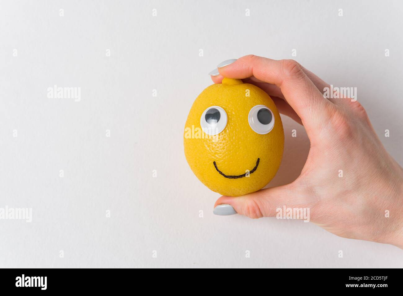 Divertente limone con occhi e sorriso su sfondo bianco. La mano della donna  che tiene un sorriso di limone Foto stock - Alamy