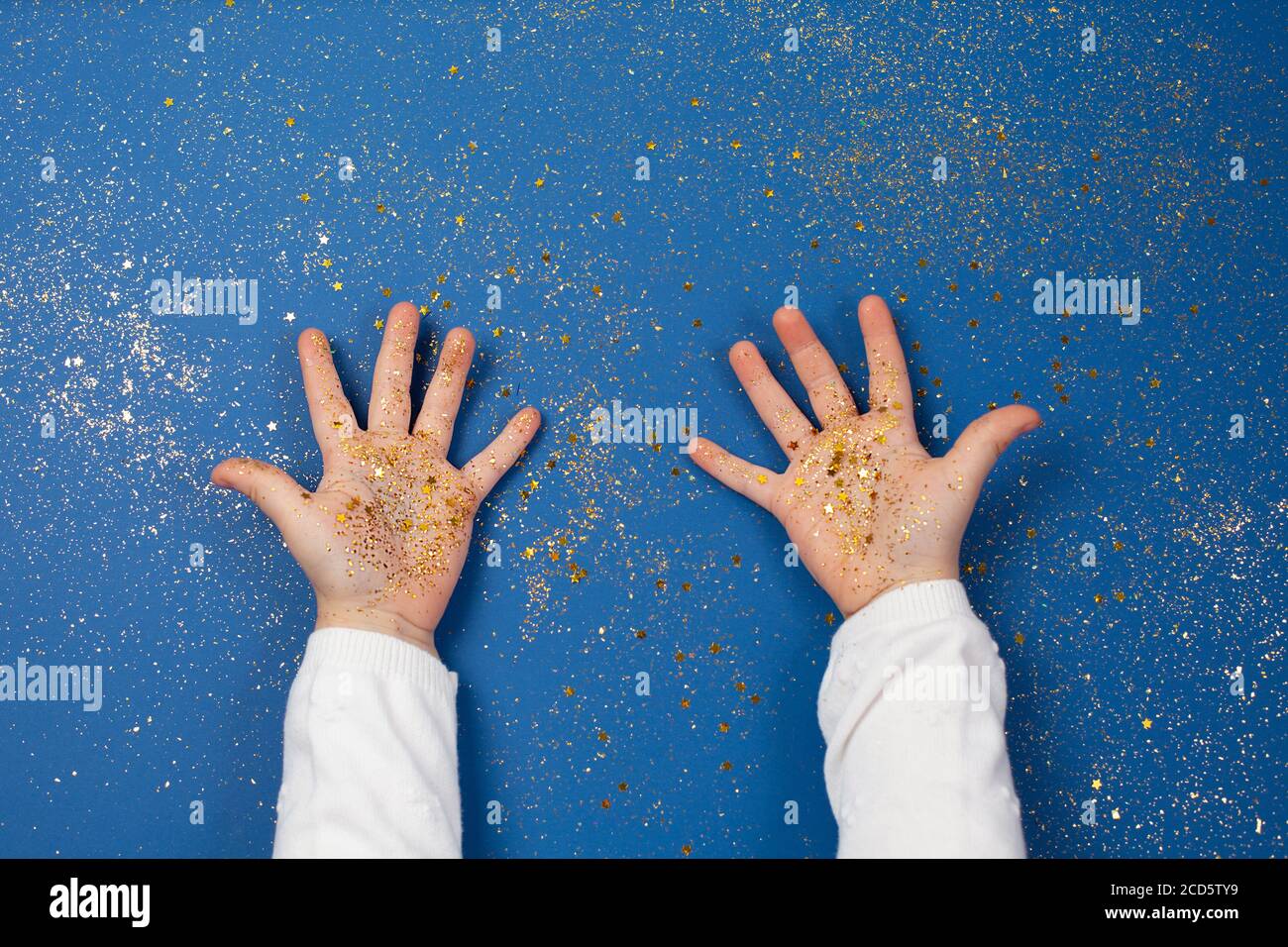 Le mani del bambino che tengono le stelle dorate su sfondo blu scintillante. Foto Stock