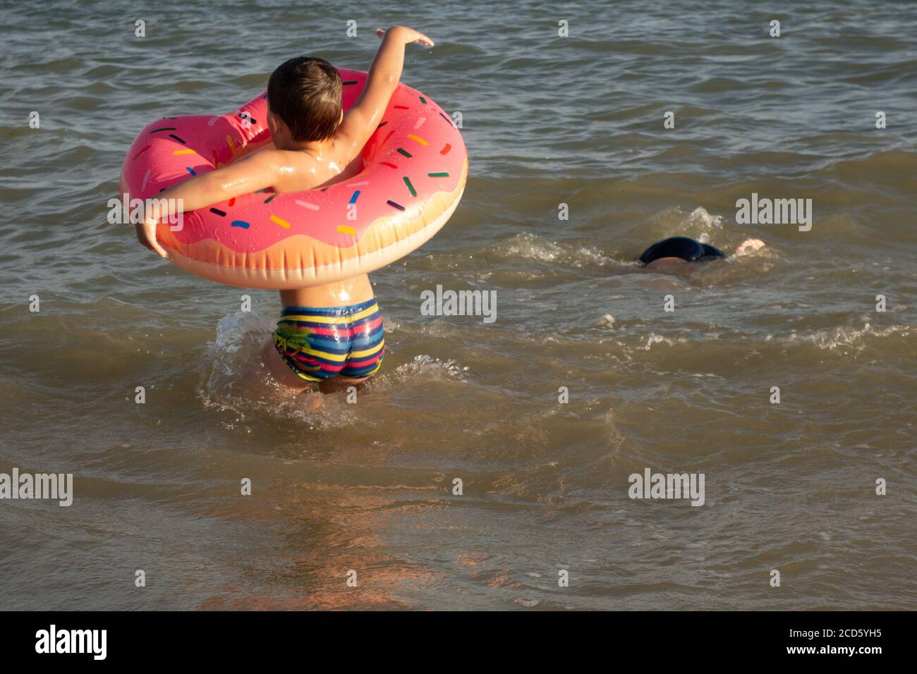 Un ragazzo di 5 anni bagna in un anello di vita a forma di ciambella in una giornata di sole. Foto Stock