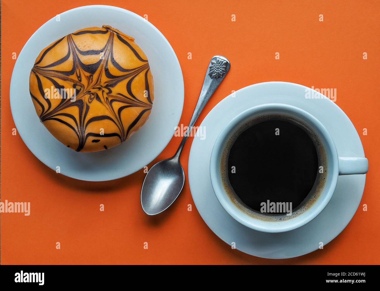 Ciambella di Halloween arancione con ragnatela e tazza bianca di caffè su sfondo arancione. Scatto in testa. Foto Stock