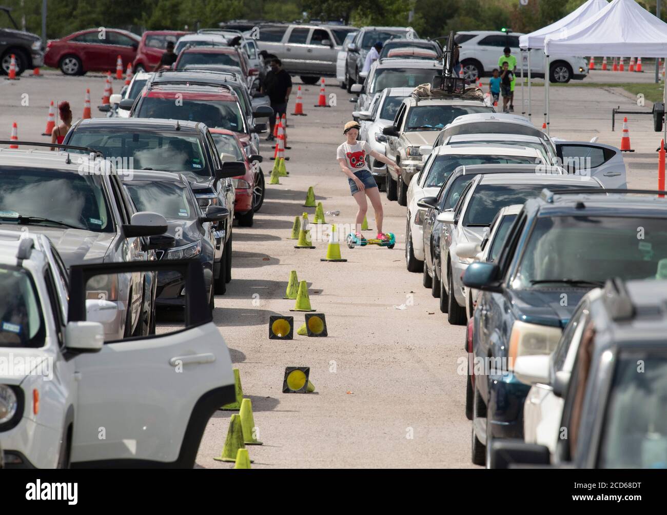 Austin, Texas USA 26 agosto 2020: Centinaia di auto dalla costa orientale del Texas e sud-ovest della Louisiana aspettano in fila un centro di evacuazione dell'uragano Laura presso l'area di parcheggio del circuito delle Americhe. Dopo aver trascorso ore a bordo del veicolo di famiglia, questo bambino ottiene un po' di aria fresca guidando uno scooter hoverboard autobilanciato. Laura dovrebbe fare la caduta di terra durante la notte come una tempesta di categoria 4 e devastare lungo le coste del Texas e della Louisiana e l'entroterra. Credit: Bob Daemmrich/Alamy Live News Foto Stock