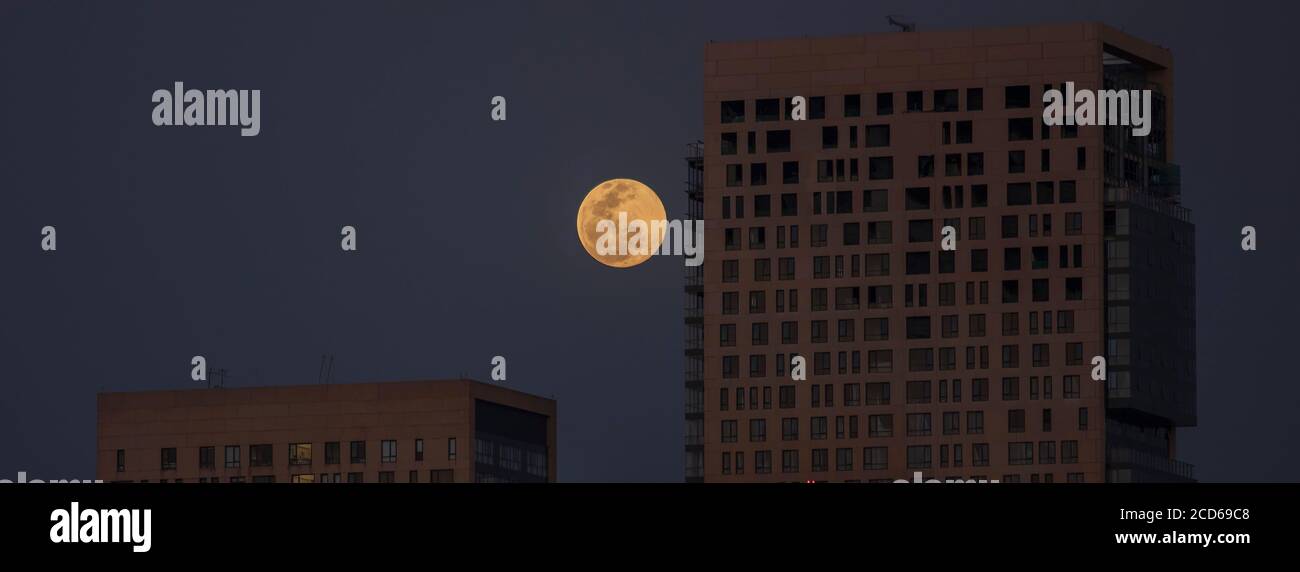 Luna piena in aumento vista tra gli edifici Foto Stock