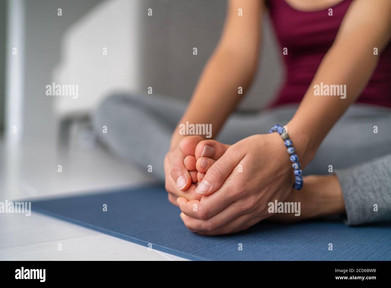 Yoga gamba allunga la donna a casa. Gambe a farfalla seduta allungano tenendo insieme le suole dei piedi. Closeup di mani che tengono i piedi nudi sul tappetino per esercizi Foto Stock