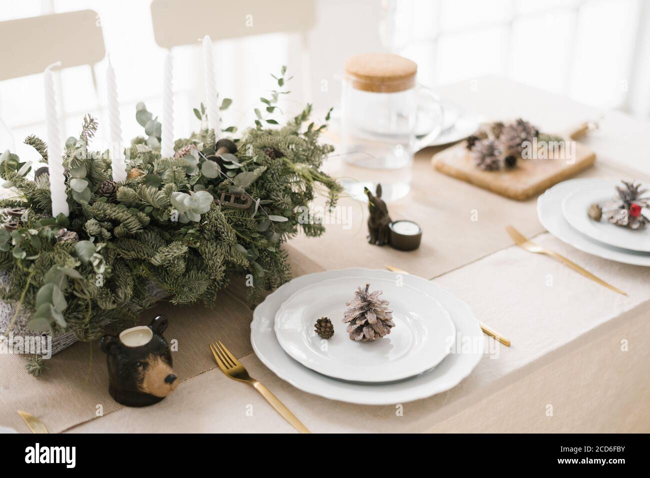 Elegante tavolo di Natale: Una composizione di rami di abete, piatti bianchi decorati con coni Foto Stock