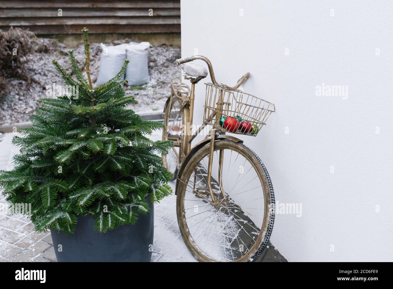Una bicicletta decorativa in bronzo con un cesto contenente palle di Natale si trova vicino all'albero di Natale sulla strada invernale vicino alla casa. Natale dic Foto Stock