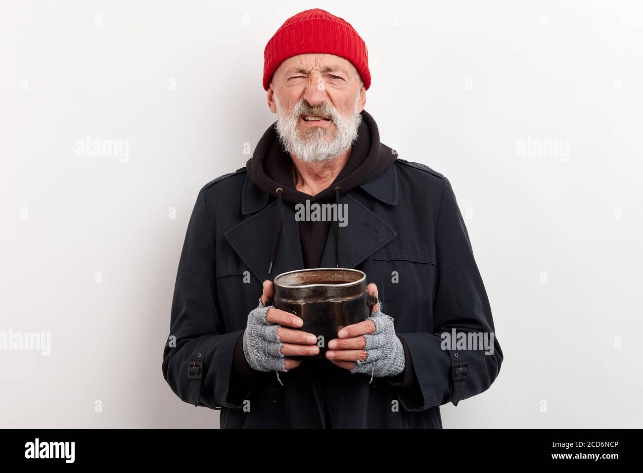 Il bum maturo in cappotto nero e il cappuccio rosso sulla testa che tiene la lattina di ferro per sollevare i soldi. Isolato su sfondo bianco Foto Stock