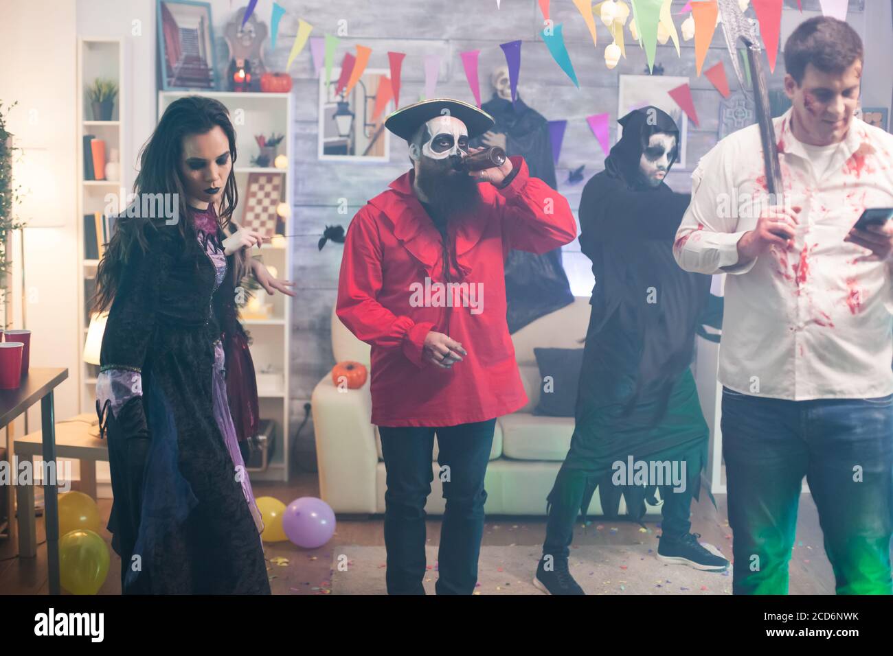 Uomo vestito come uno zombie con un'ascia utilizzando smartphone alla festa di Halloween. Foto Stock