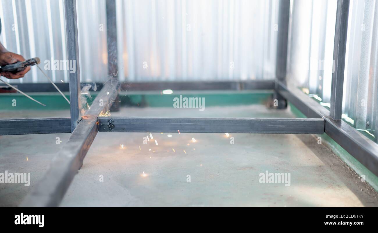 L'uomo che lavora sta saldando con torcia e casco protettivo parte intetallica in fabbrica. Foto Stock