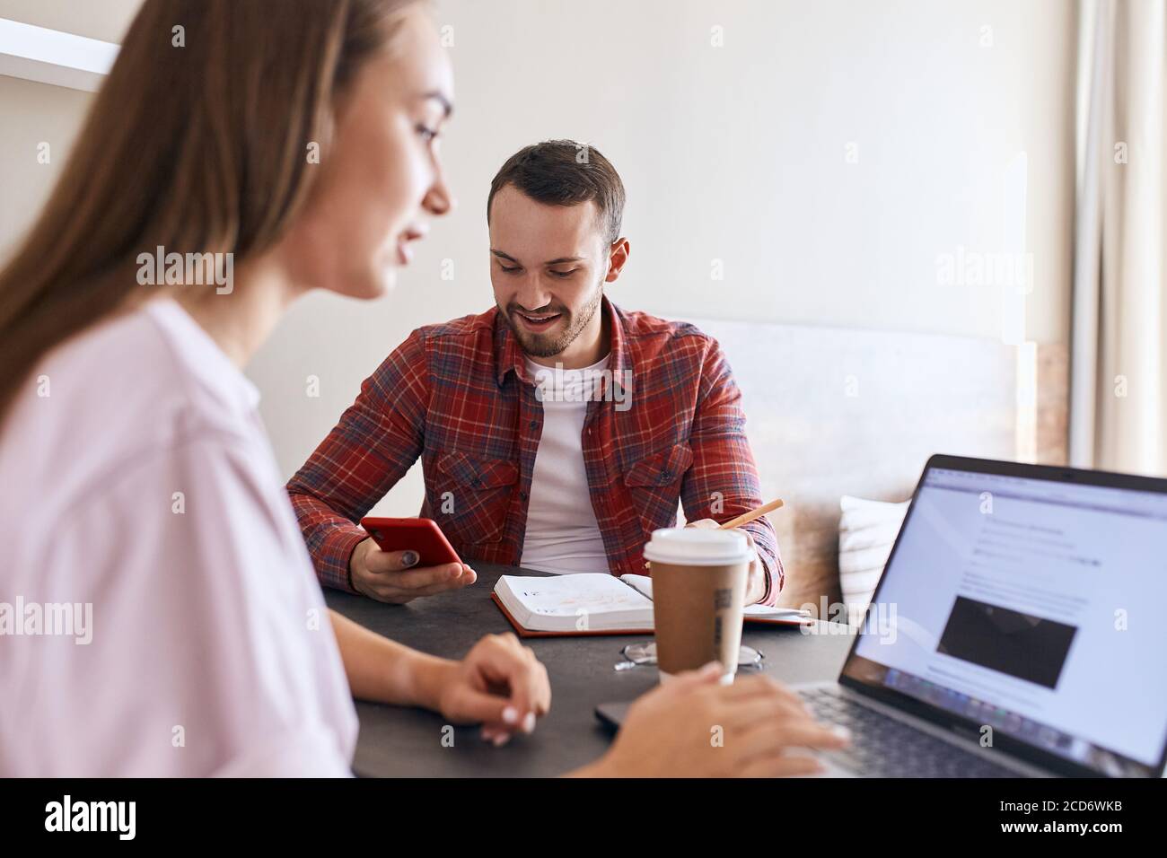 L'uomo bello e impressionante indossa una camicia rossa e una maglietta bianca, tiene il telefono cellulare rosso, si concentra nel dispositivo con il volto felice, felice di ricevere un buon massaggio da Foto Stock