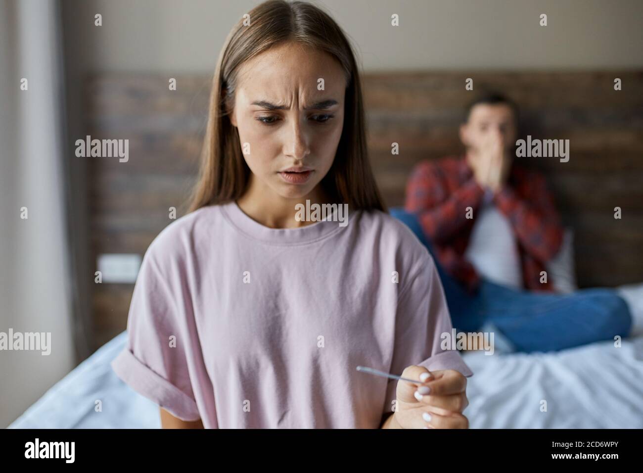 Primo piano di giovane bella ragazza con lunghi capelli belli, tiene in mano test di gravidanza, scioccato dai risultati, guardando via con paura, non sa cosa t Foto Stock