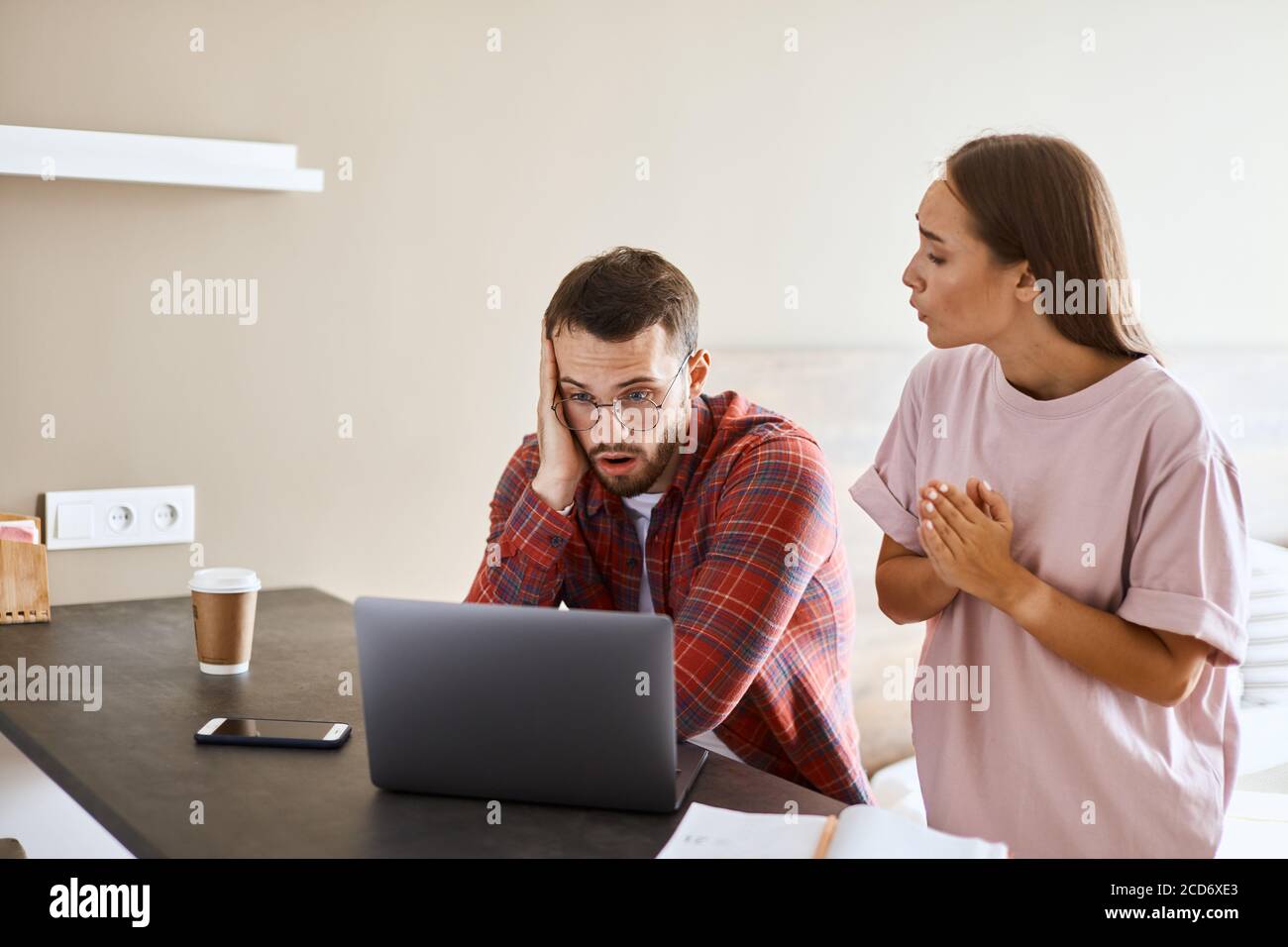 Preoccupato giovane marito looks a schermo del laptop con sentimenti sconvolgente, esprime shock leggero, gentile moglie cerca di sostenere, guarda via, esprime simpatia, Foto Stock