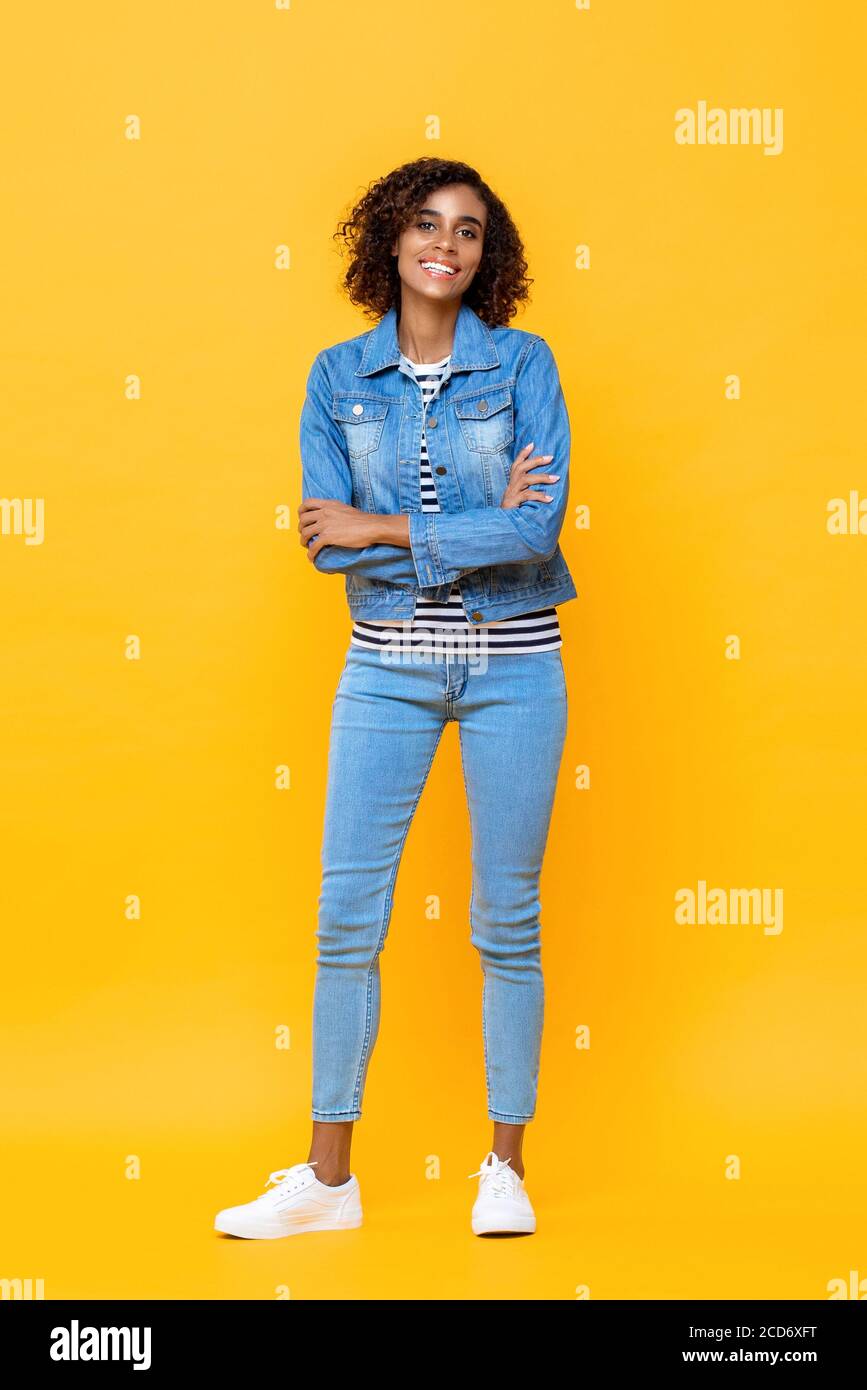 Ritratto a lunghezza intera di giovane donna afroamericana sorridente in piedi con braccia incrociate su sfondo studio giallo Foto Stock