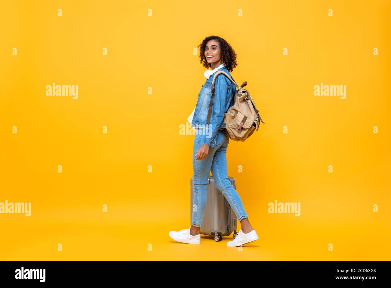 Ritratto di viaggio a tutta lunghezza di una giovane donna afro-americana stupita backpacker che cammina con i bagagli sullo sfondo giallo studio Foto Stock