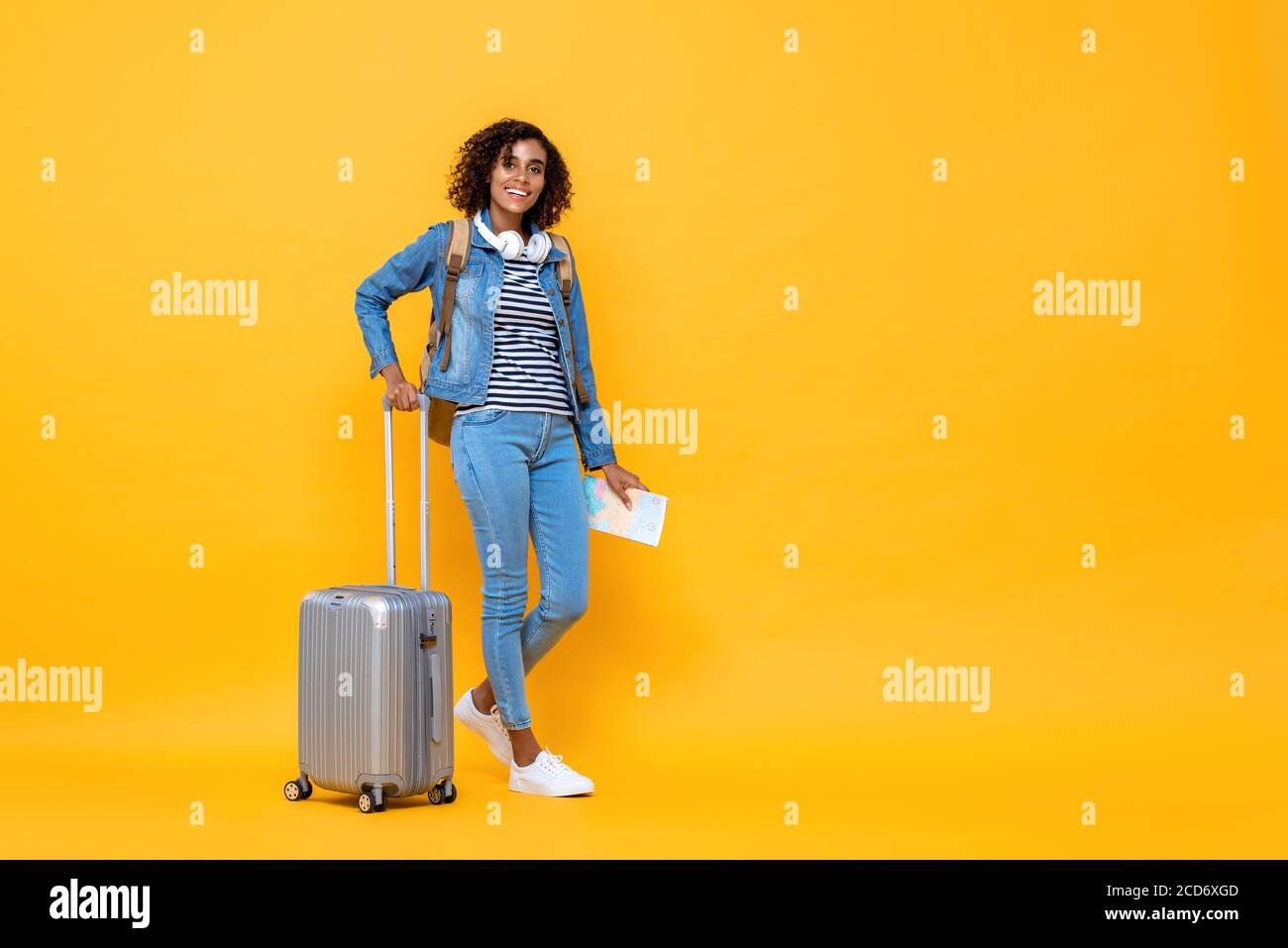 Ritratto di viaggio a tutta lunghezza di una giovane donna afroamericana sorridente backpacker in piedi e tenendo i bagagli su sfondo giallo studio Foto Stock