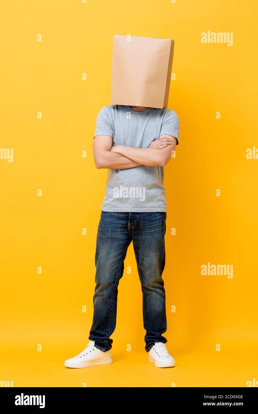 Concept ritratto a lunghezza intera dell'uomo anonimo con testa coperta con sacchetto di carta che fa le braccia incrociate gesto in studio giallo sfondo Foto Stock