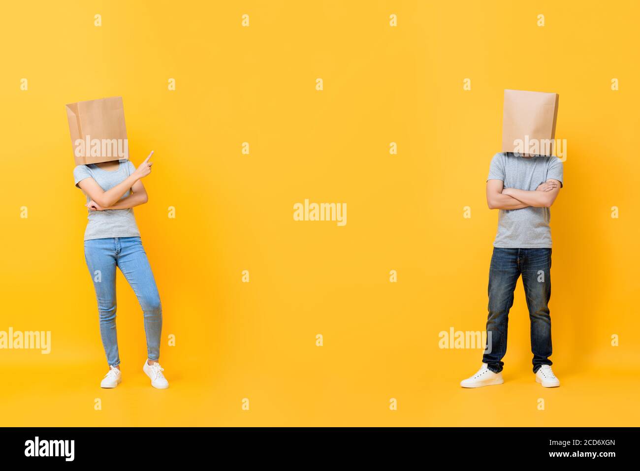 Ritratto a lunghezza intera di coppia anonima senza volto che copre le teste con sacchetti di carta che presentano spazio tra isolati su sfondo giallo studio Foto Stock