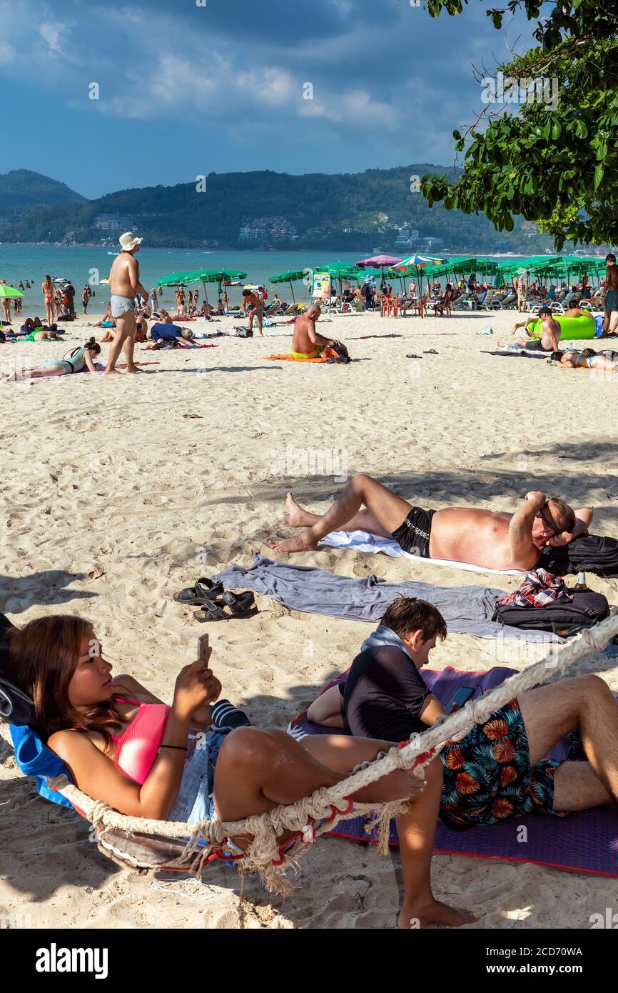 Turista in amaca usando un telefono mobile sulla spiaggia, Patong, Phuket, Thailandia Foto Stock