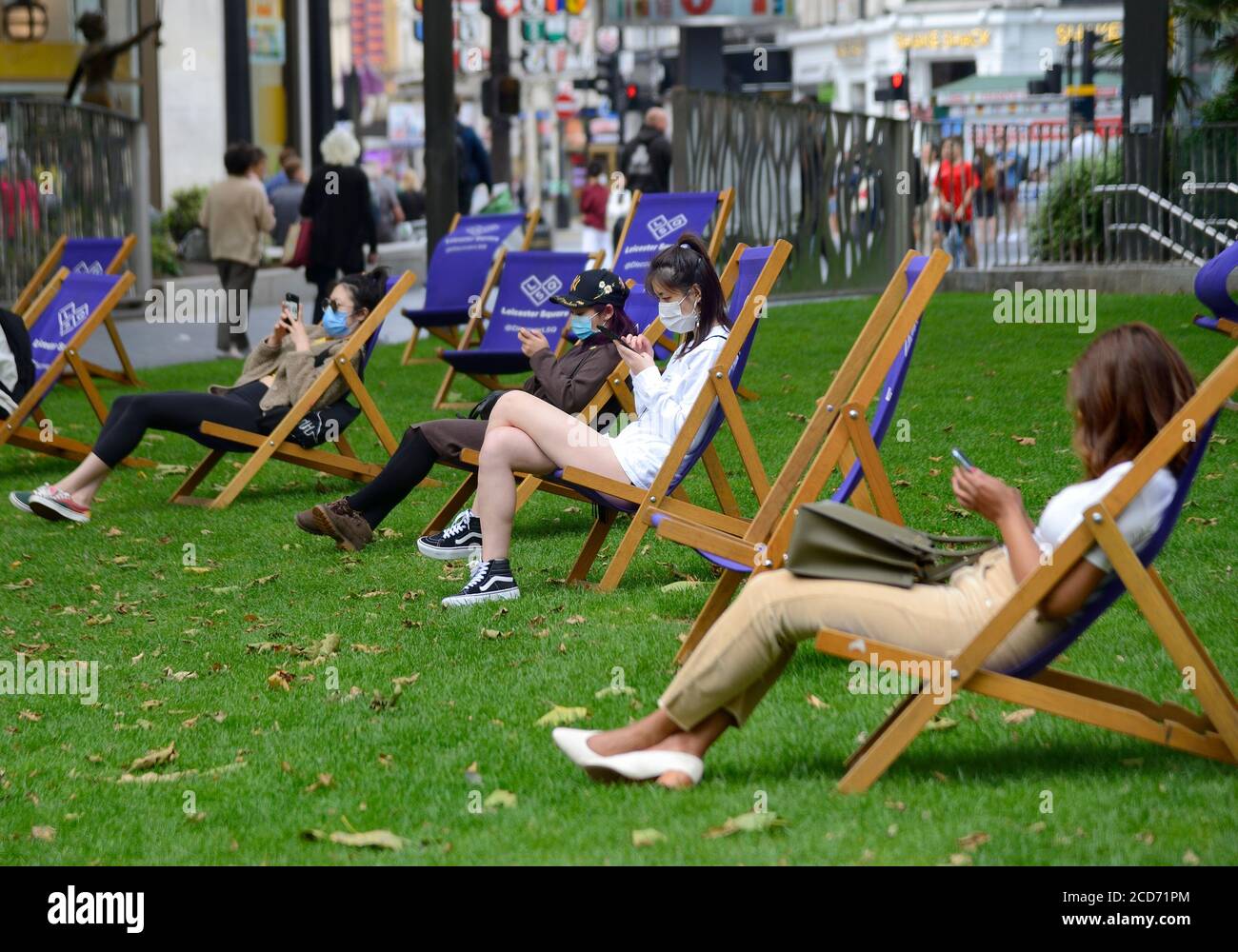 Londra, Inghilterra, Regno Unito. Giovani donne che indossano maschere facciali e utilizzano i loro telefoni in Leicester Square durante la pandemia COVID, agosto 2020 Foto Stock