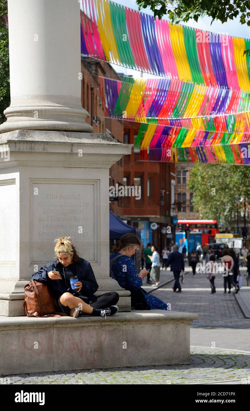 Londra, Inghilterra, Regno Unito. Giovane donna con caffè sul suo cellulare, e arcobaleno decorazioni in sette Dials Foto Stock