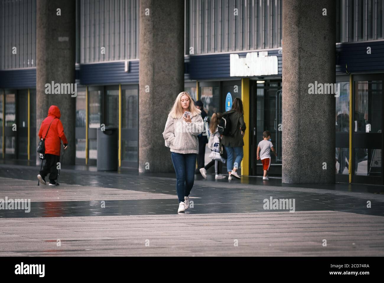 Giovane donna che guarda il suo telefono mentre esce dalla stazione degli autobus Preston a Lancashire, Regno Unito. Foto Stock