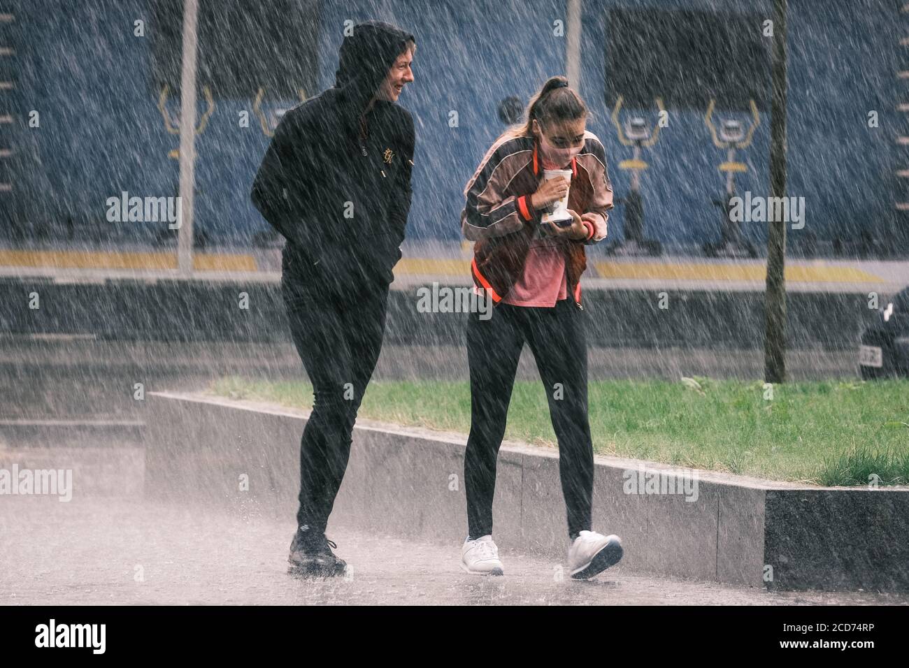 UK Weather: Giovani donne che indossano una maschera facciale e giovane uomo catturato in una doccia a pioggia pesante, Preston, UK Foto Stock