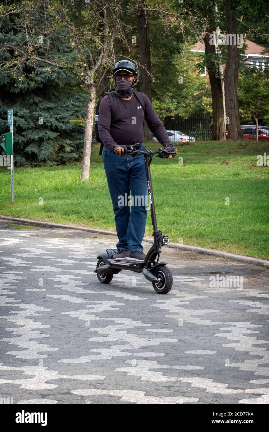 Un uomo che indossa un casco di sicurezza e una sciarpa da collo solleva il  suo scooter elettrico Nanrobot su un percorso nel Kissena Park a Flushing,  Queens, New York City Foto